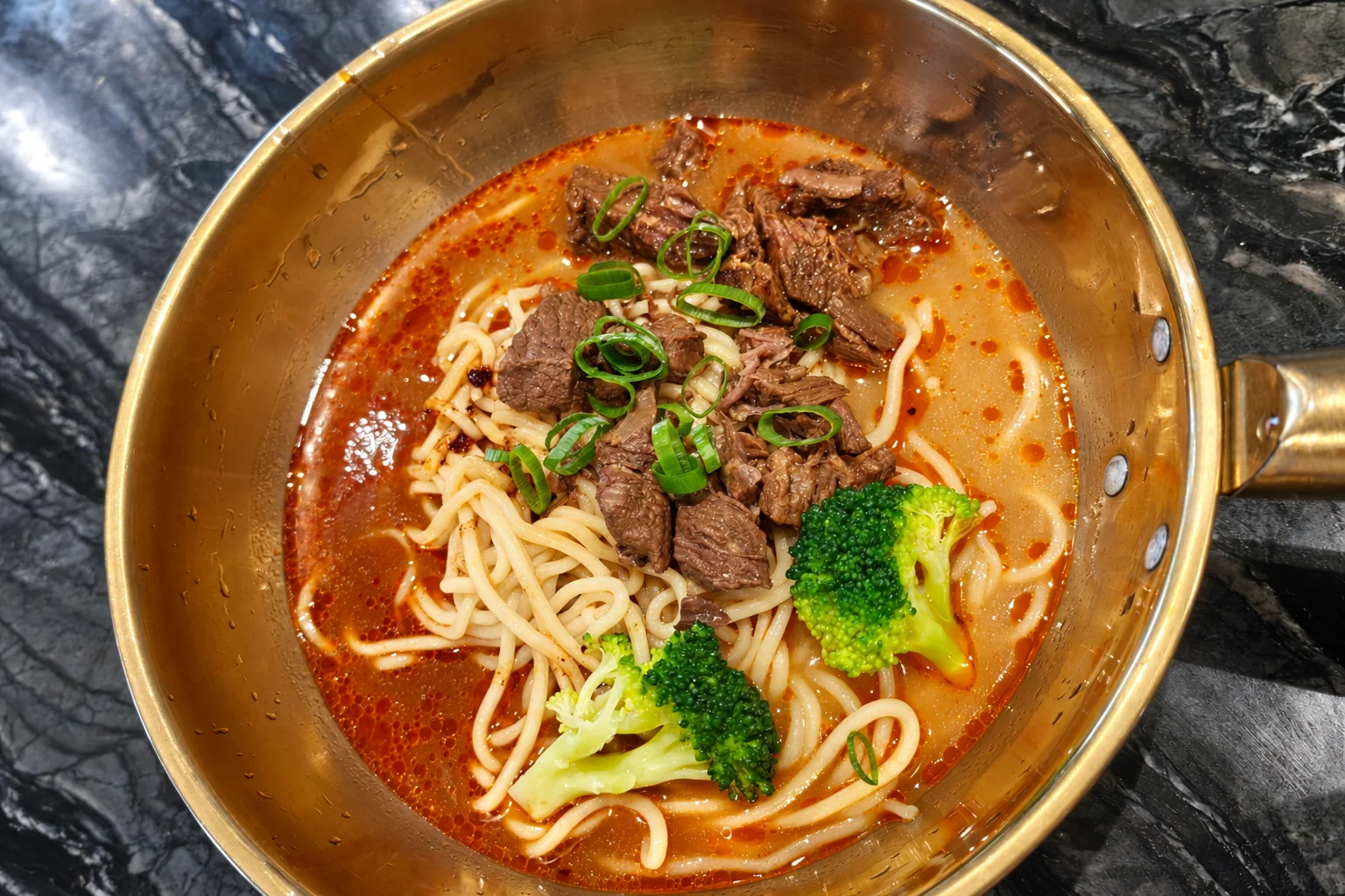 Beef noodle soup in a small golden pot: braised beef chunks, spring onion, broccoli, spicy broth