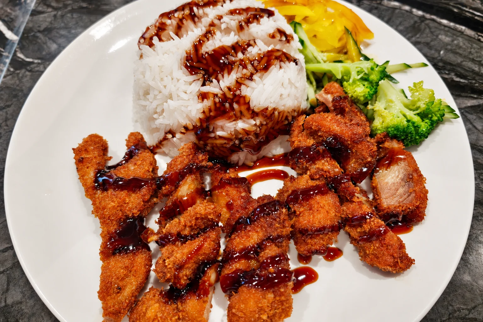 Crispy chicken rice: sliced breaded chicken with sauce, white rice, broccoli and vegetables, white plate