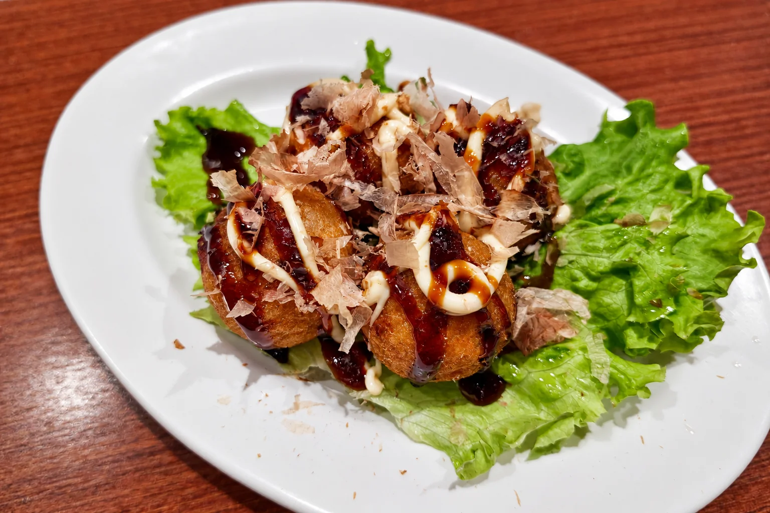Octopus balls with sauce and mayonnaise, bonito flakes, on lettuce, white plate